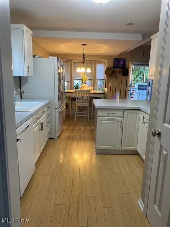 Kitchen with dishwasher, a sink, a peninsula, light countertops, and white cabinets