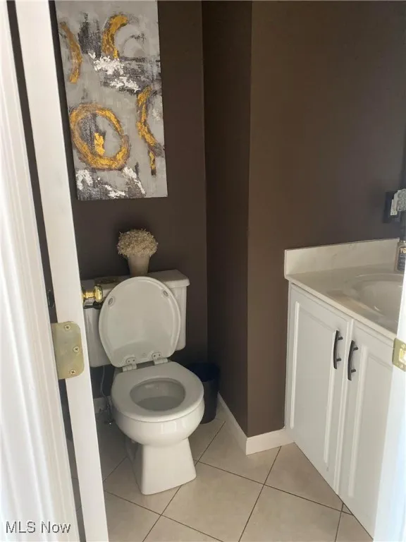 Half bath featuring toilet, baseboards, tile patterned floors, and vanity