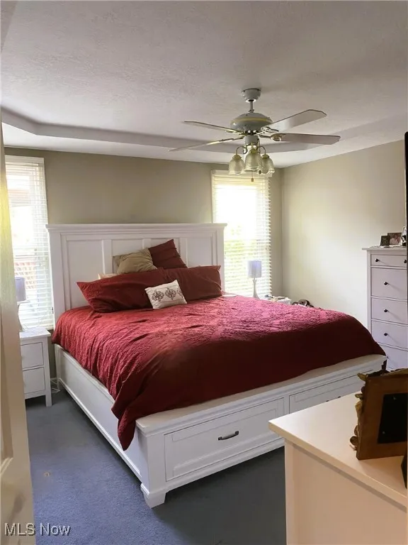 Bedroom featuring a textured ceiling, a ceiling fan, and dark carpet