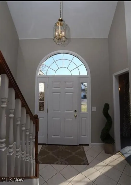 Entryway with stairs, a chandelier, light tile patterned flooring, and high vaulted ceiling