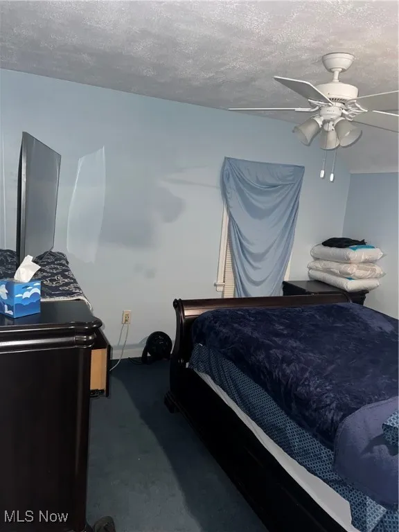 Carpeted bedroom with baseboards, ceiling fan, and a textured ceiling