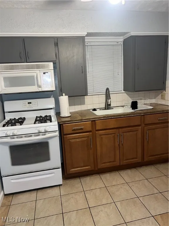 Kitchen with brown cabinetry, light tile patterned flooring, refrigerator, decorative backsplash, and a ceiling fan