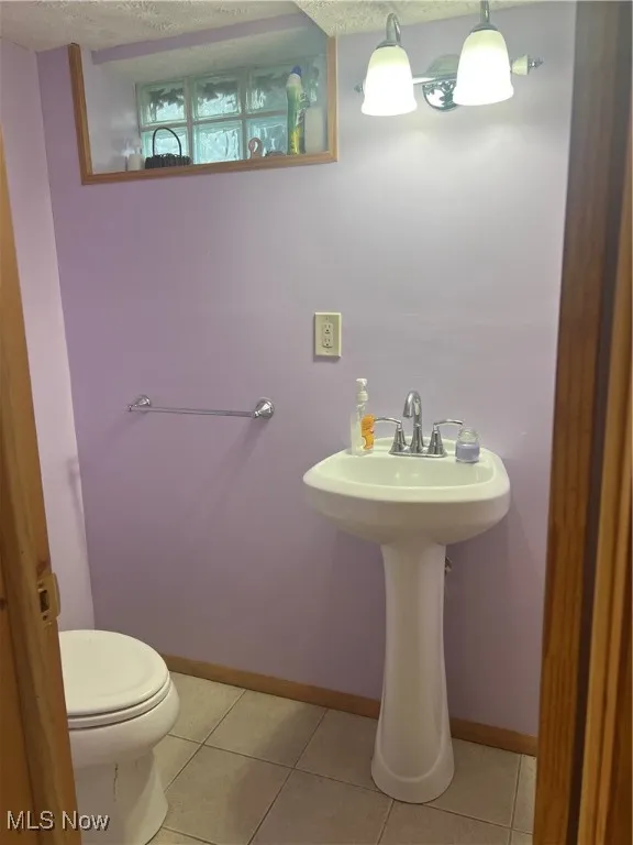 Half bathroom with toilet, tile patterned floors, baseboards, and a sink
