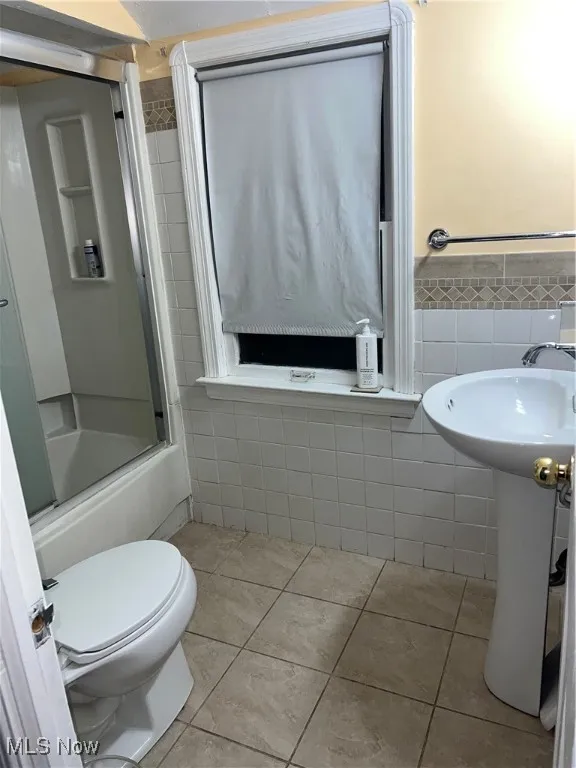 Full bath featuring tile patterned flooring, tile walls, toilet, and enclosed tub / shower combo