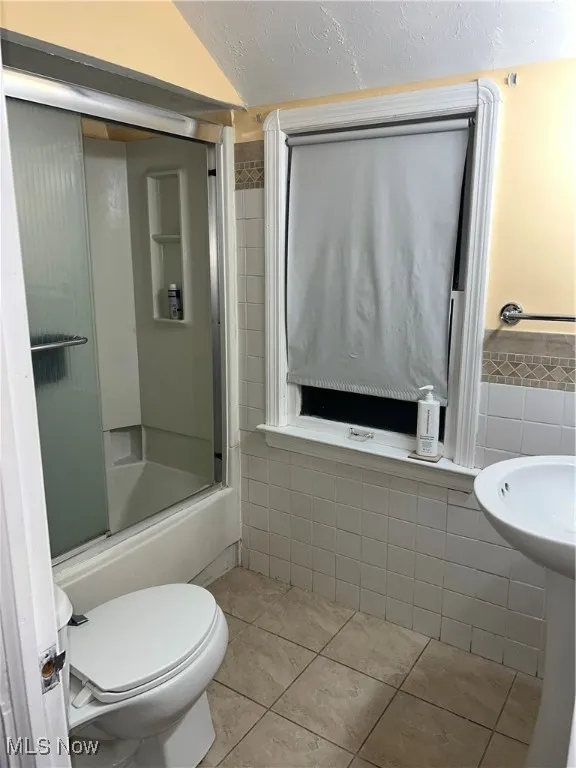 Full bath featuring tile patterned flooring, tile walls, toilet, and enclosed tub / shower combo