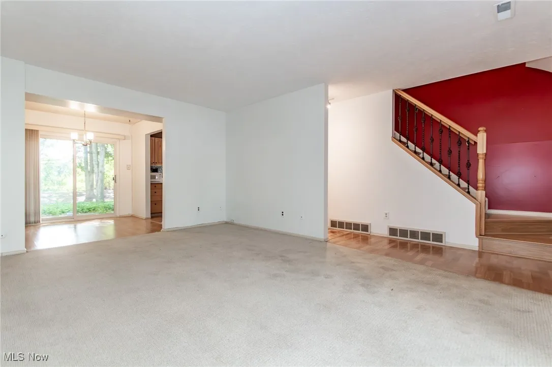Unfurnished living room with carpet flooring, a chandelier, and stairs