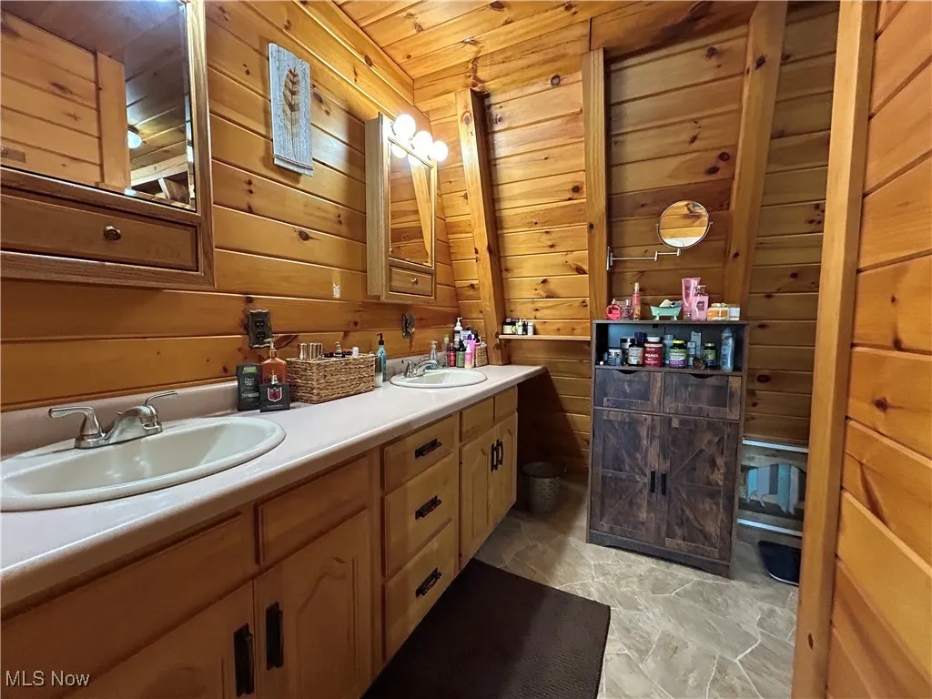 Full bath featuring a sink, double vanity, and wooden walls