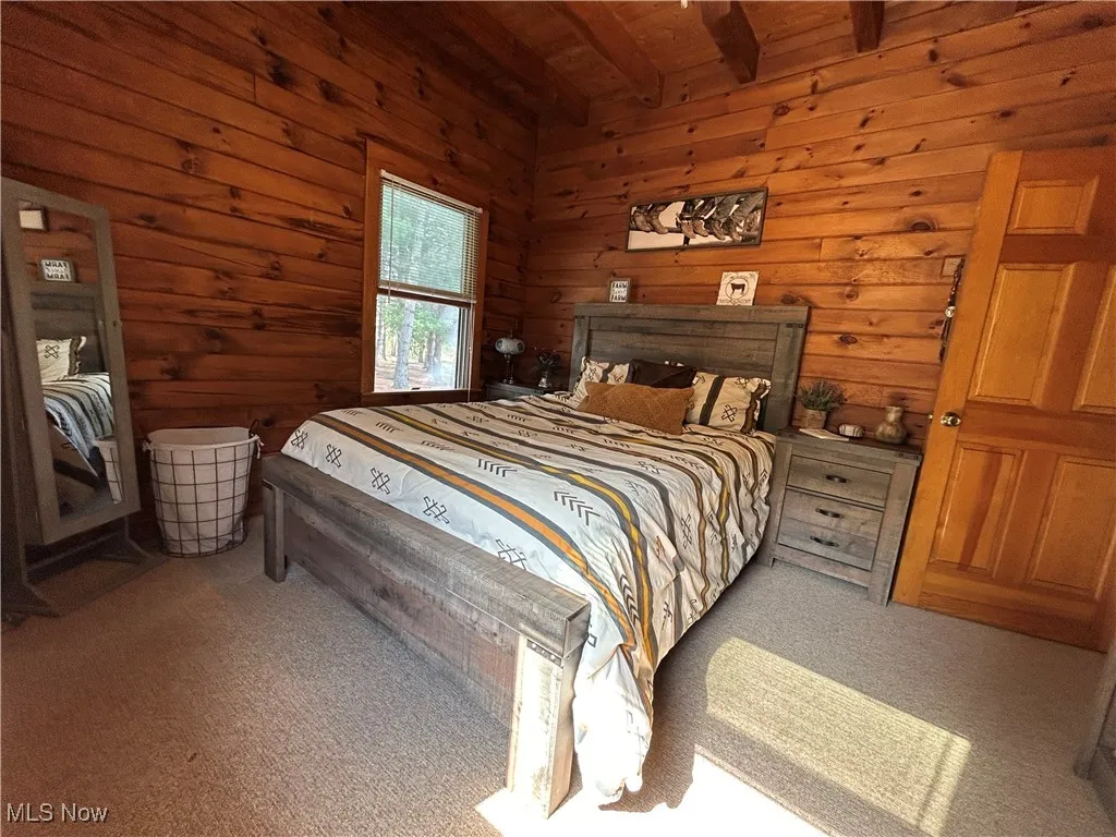 Carpeted bedroom featuring wooden walls, wood ceiling, and beamed ceiling