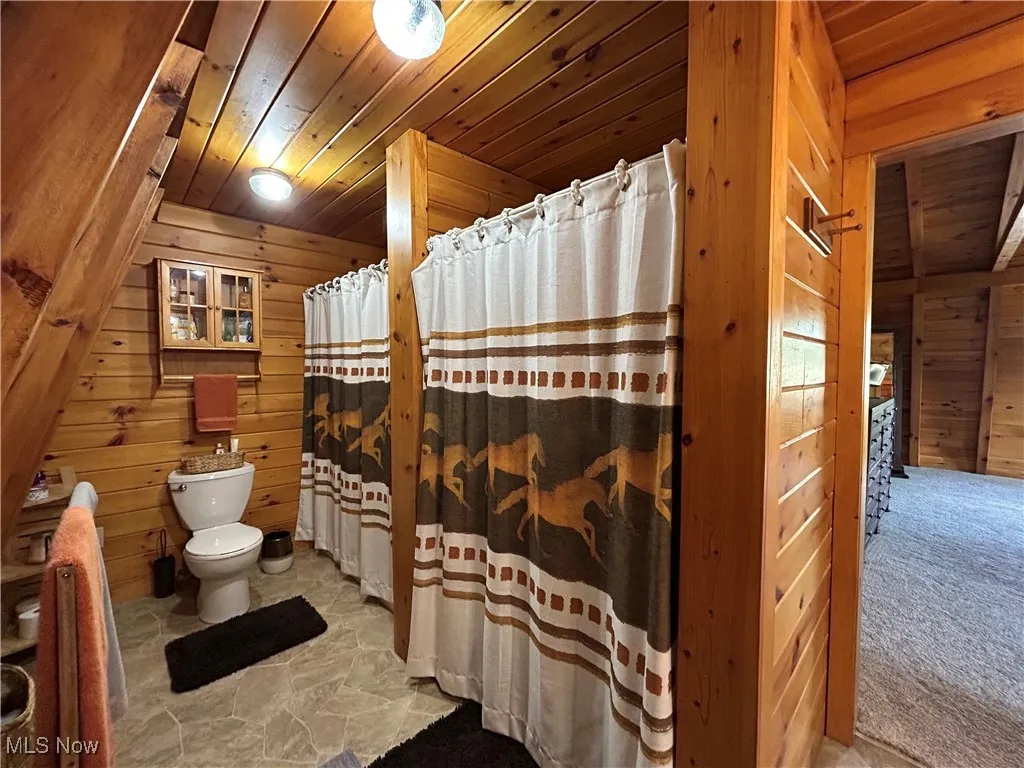 Full bath featuring toilet, stone finish flooring, wood ceiling, a shower with shower curtain, and wooden walls