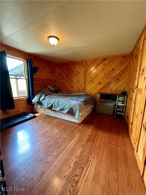 Unfurnished bedroom with wood finished floors, a textured ceiling, and wood walls