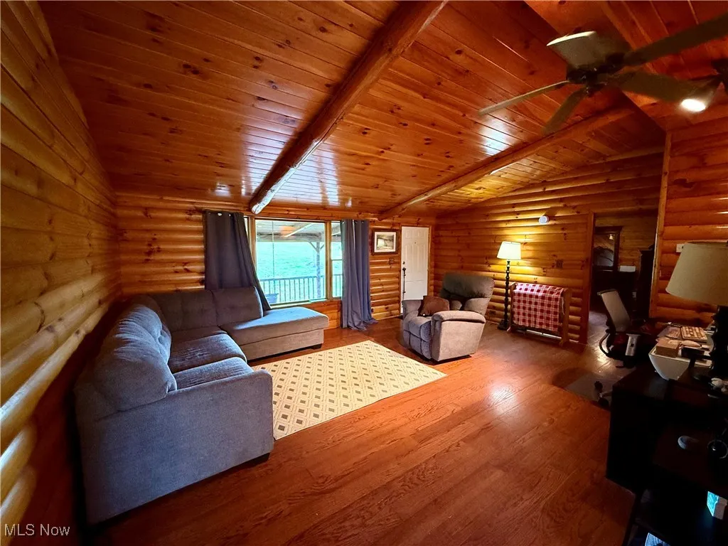 Living area with rustic walls, wood ceiling, wood finished floors, and a ceiling fan