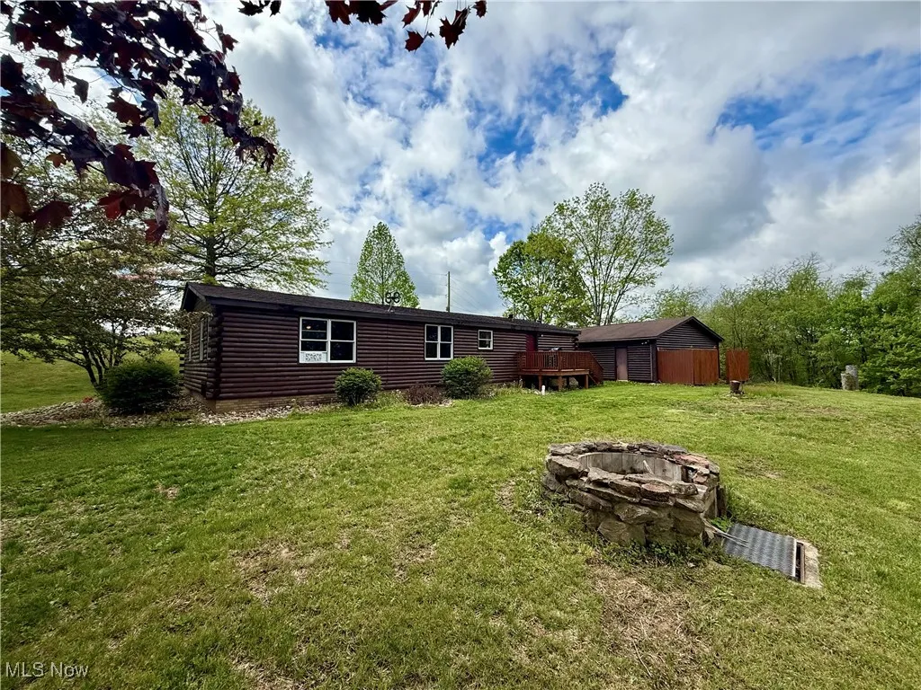 Back of property featuring an outdoor fire pit, a lawn, a deck, and log siding