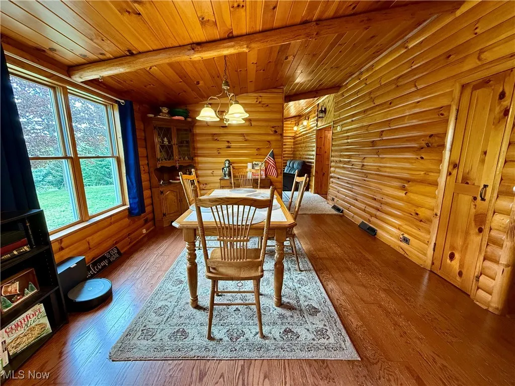 Dining space with rustic walls, a chandelier, wood ceiling, beam ceiling, and hardwood / wood-style flooring