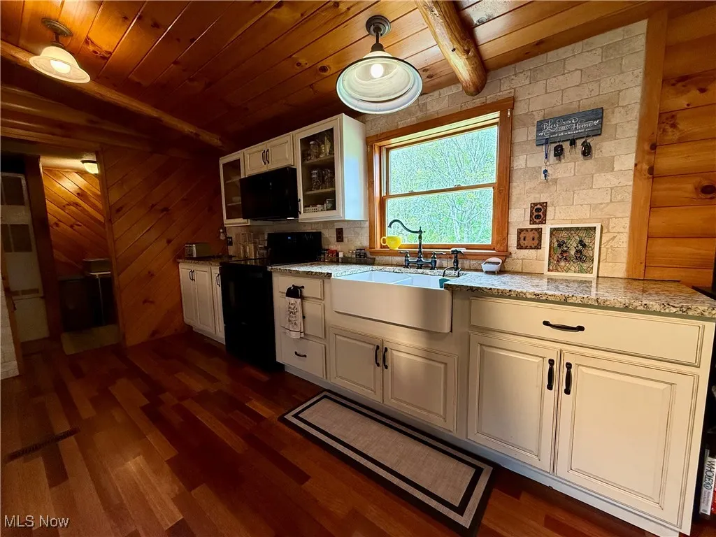 Kitchen with a sink, black appliances, wooden ceiling, glass insert cabinets, and dark wood finished floors