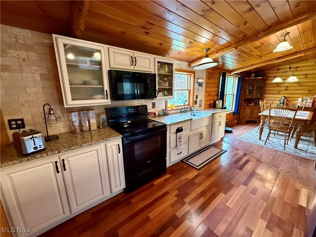 Kitchen with black appliances, wood ceiling, dark wood-type flooring, white cabinets, and light stone counters