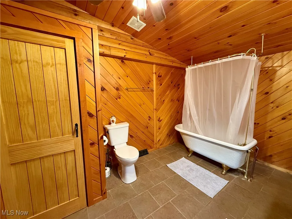Full bath featuring lofted ceiling, toilet, a freestanding bath, wooden walls, and wood ceiling
