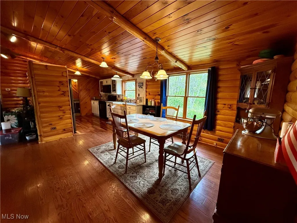 Dining area with log walls, wood finished floors, wooden ceiling, a chandelier, and beam ceiling