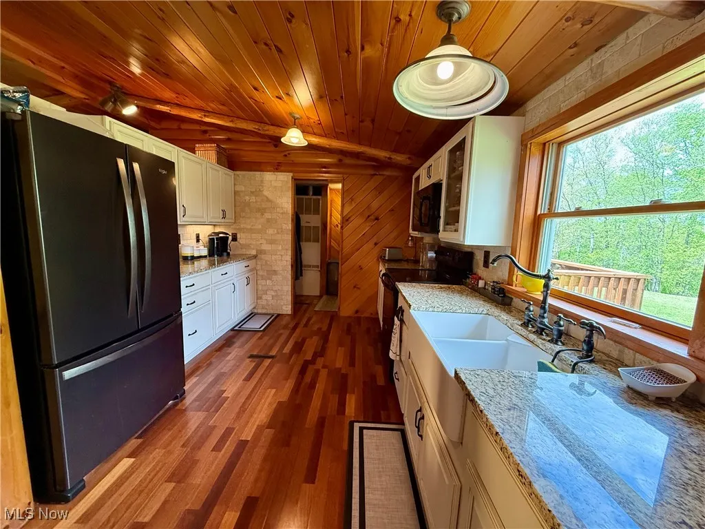 Kitchen featuring black appliances, plenty of natural light, wood ceiling, white cabinetry, and a sink