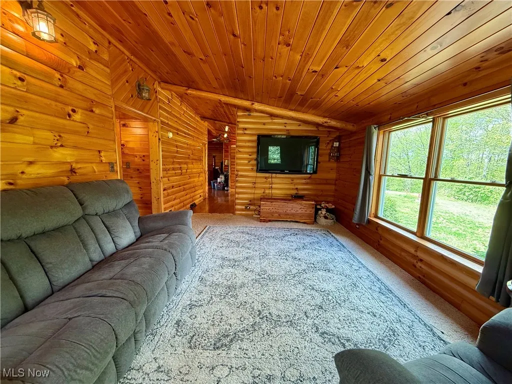 Living room featuring lofted ceiling, wooden ceiling, log walls, and carpet flooring