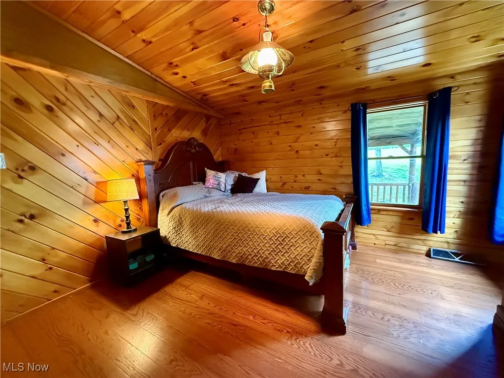 Bedroom featuring vaulted ceiling, wooden ceiling, wood finished floors, and wooden walls