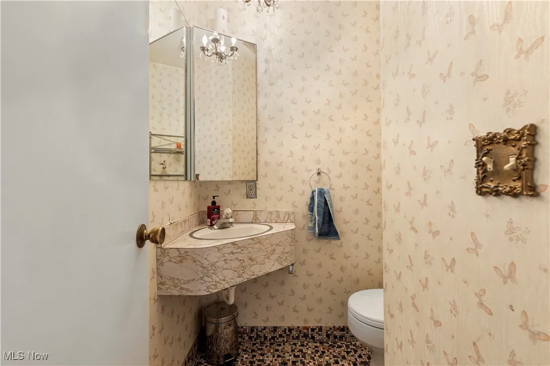 Bathroom featuring toilet, wallpapered walls, and a sink