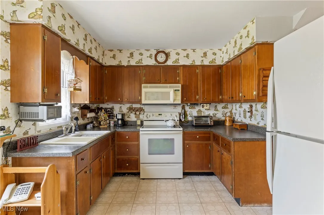 Kitchen featuring brown cabinets, white appliances, dark countertops, and a sink