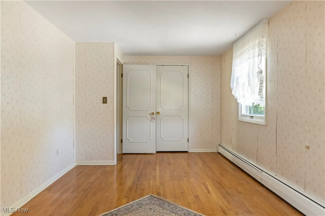 Unfurnished bedroom featuring baseboard heating and wood finished floors