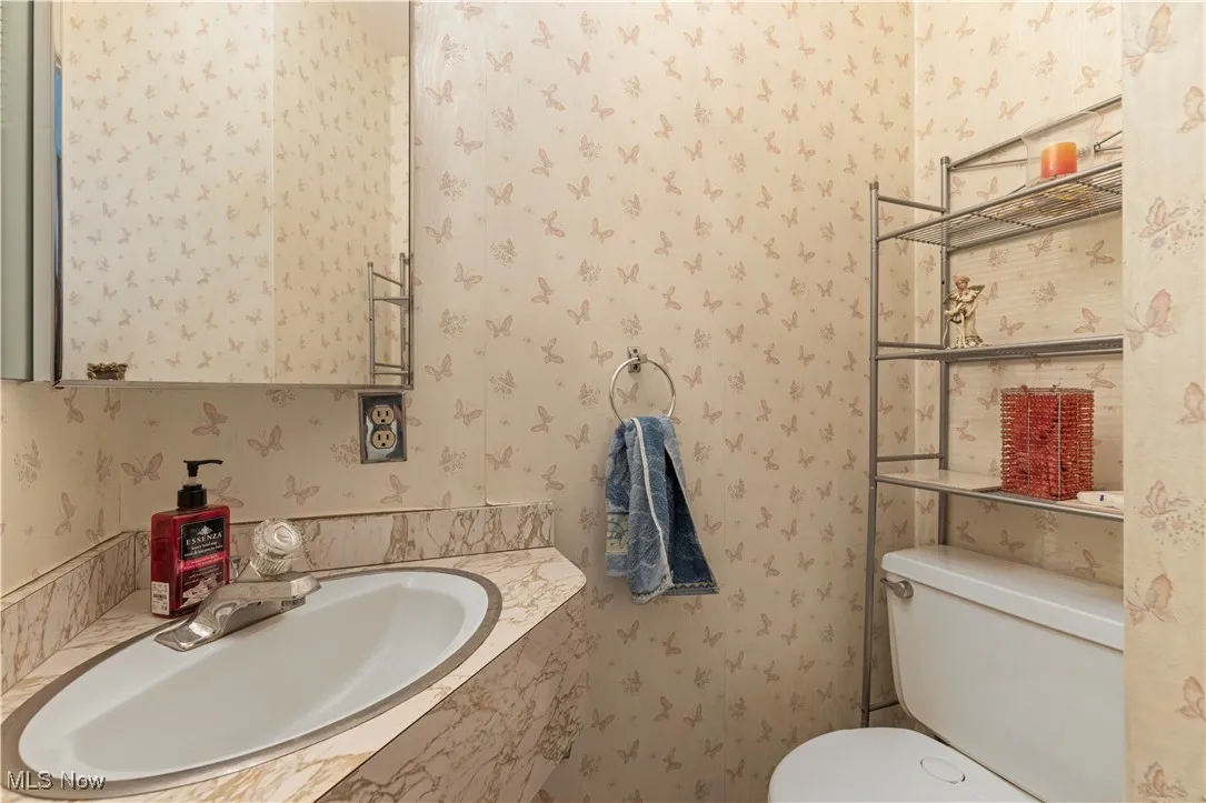 Bathroom with toilet, wallpapered walls, and a sink