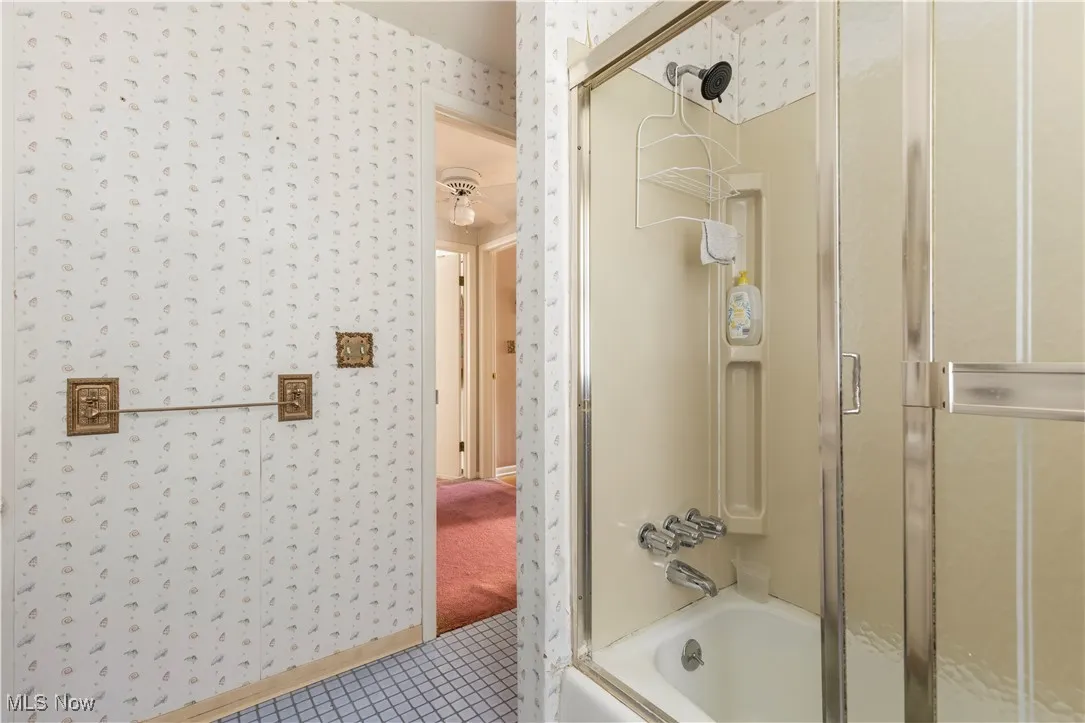 Bathroom with enclosed tub / shower combo, tile patterned flooring, and wallpapered walls