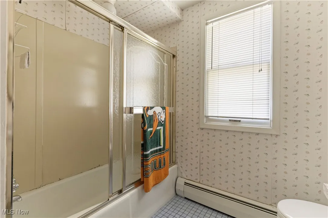 Bathroom featuring toilet, enclosed tub / shower combo, wallpapered walls, tile patterned floors, and a baseboard heating unit