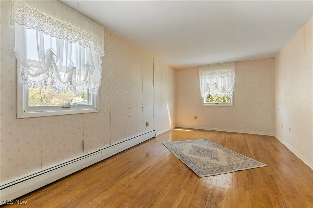 Unfurnished room with a baseboard radiator, wallpapered walls, and wood finished floors