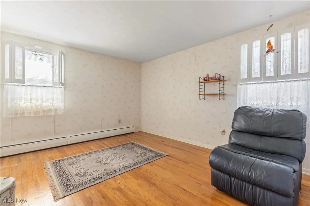Sitting room with a baseboard heating unit, a wealth of natural light, and wood finished floors
