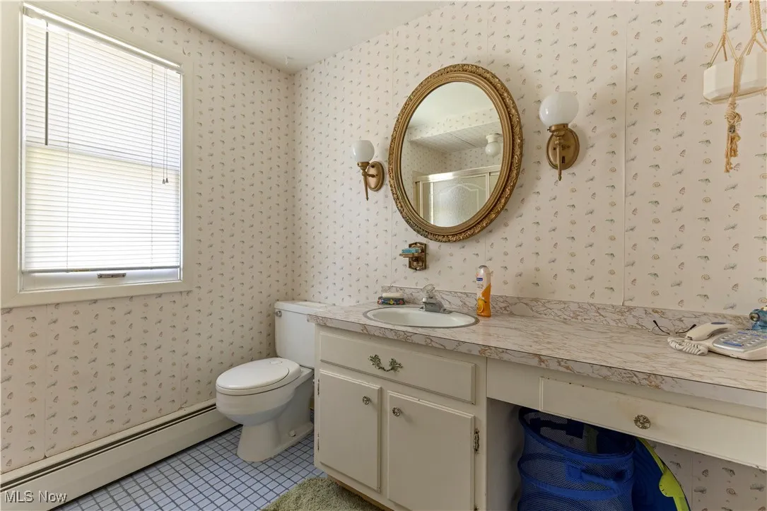 Bathroom with wallpapered walls, a baseboard heating unit, toilet, tile patterned floors, and vanity