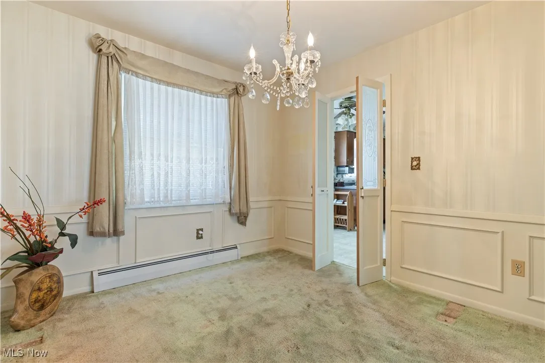 Unfurnished dining area with carpet flooring, a wainscoted wall, a notable chandelier, a decorative wall, and baseboard heating