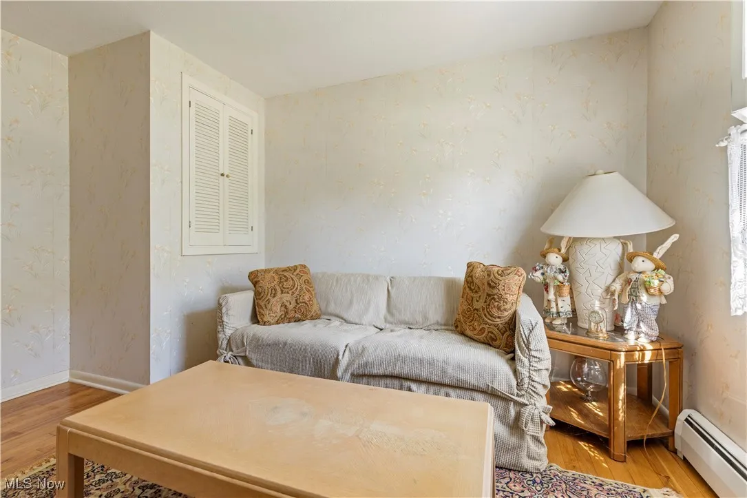 Living area with wallpapered walls, baseboard heating, and wood finished floors