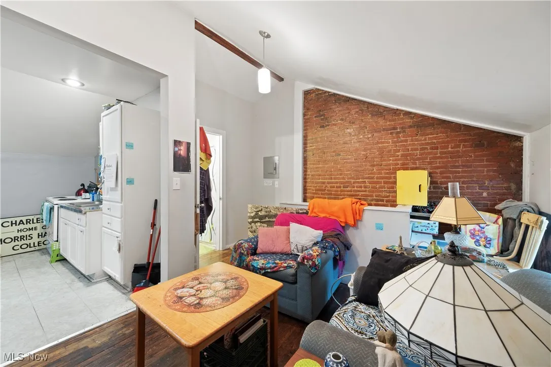 Living area featuring vaulted ceiling, brick (Up unit)  wall, and wood finished floors