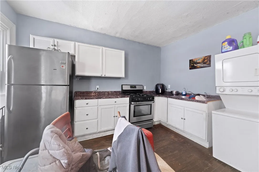Kitchen featuring appliances with (Up front unit)stainless steel finishes, stacked washing machine and dryer, white cabinets, dark wood finished floors, and a textured ceiling