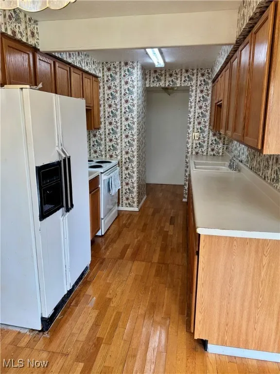 Kitchen featuring white appliances, wallpapered walls, a sink, light wood-type flooring, and light countertops