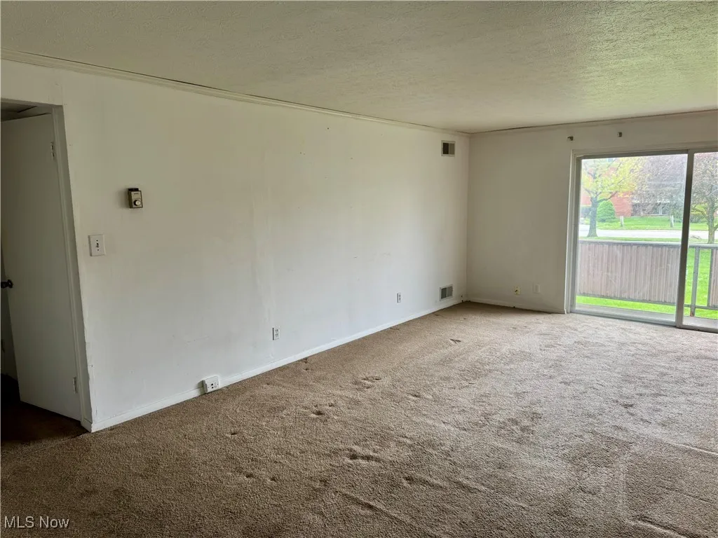 Carpeted spare room featuring a textured ceiling and baseboards