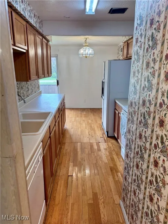 Kitchen featuring white appliances, a sink, light wood finished floors, light countertops, and brown cabinets