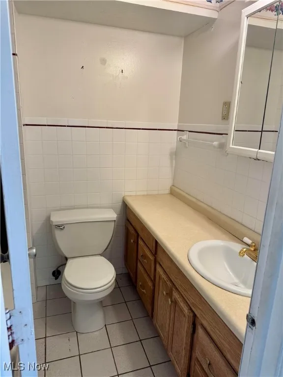 Full bathroom featuring tile walls, vanity, tile patterned flooring, toilet, and a wainscoted wall