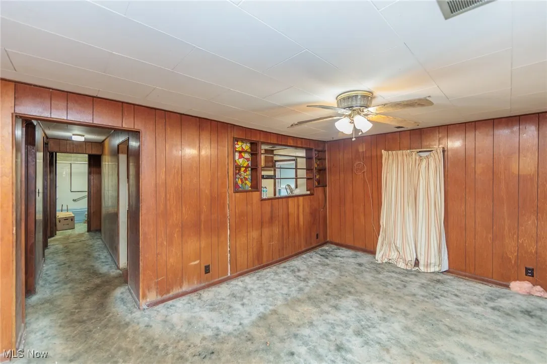 Carpeted spare room featuring wooden walls and ceiling fan