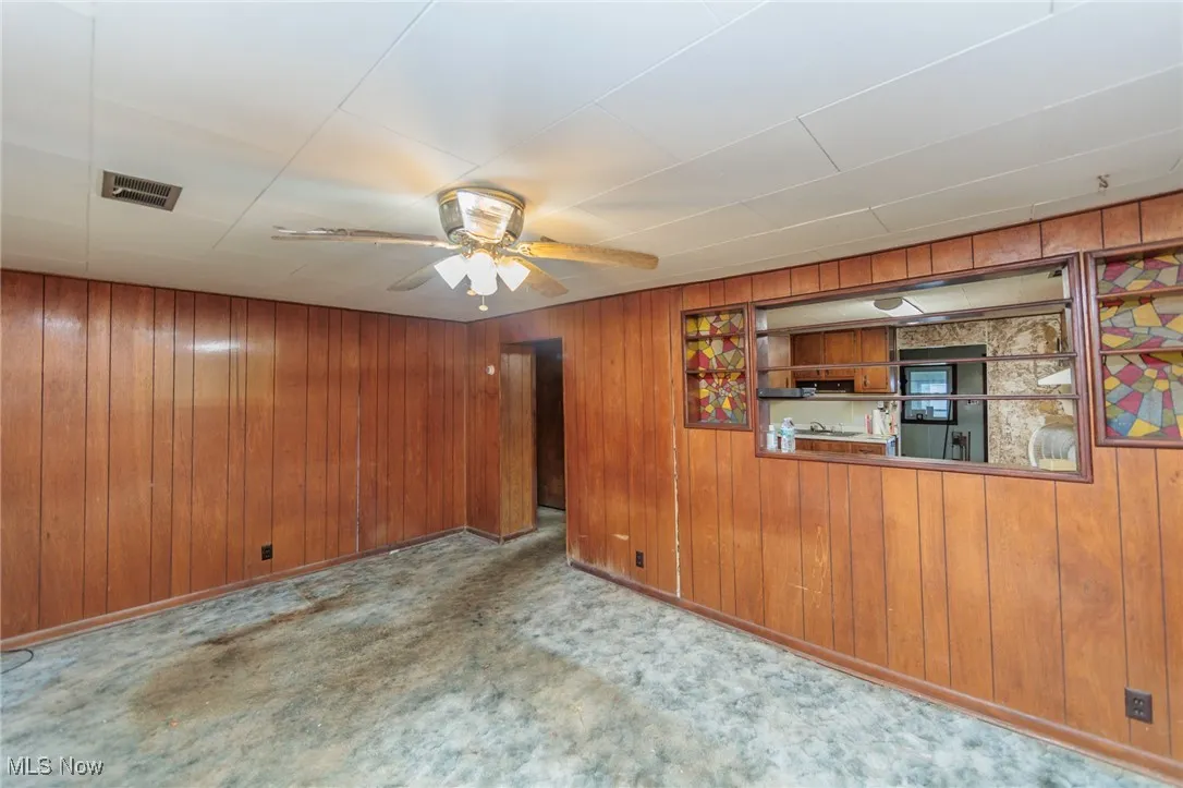 Empty room featuring light carpet, wood walls, and ceiling fan