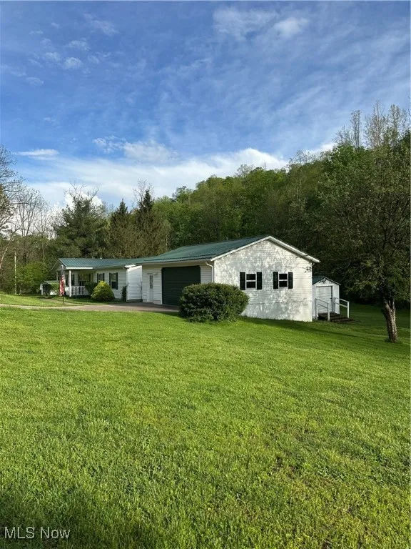 Side view of property featuring a storage shed, driveway, a yard, a garage, and metal roof