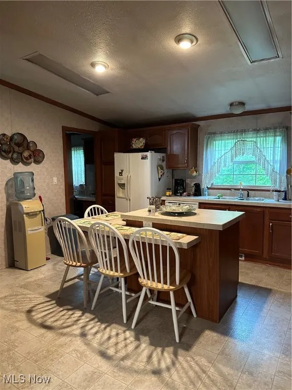 Kitchen featuring a sink, freestanding refrigerator, lofted ceiling, a kitchen island, and light countertops