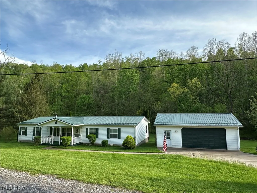 View of front of house with a forest view, a garage, an outdoor structure, and metal roof