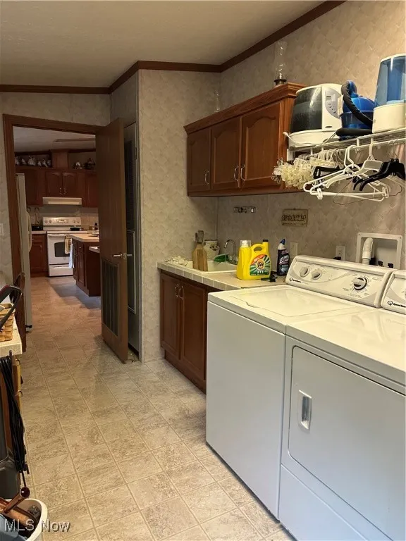 Laundry room with washing machine and clothes dryer, cabinet space, and crown molding