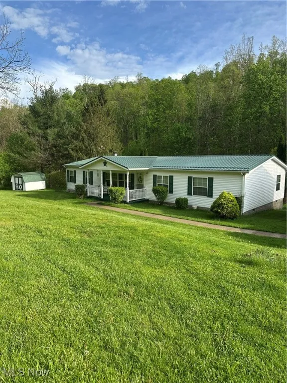 View of front facade with a porch, an outbuilding, a front lawn, and a storage shed