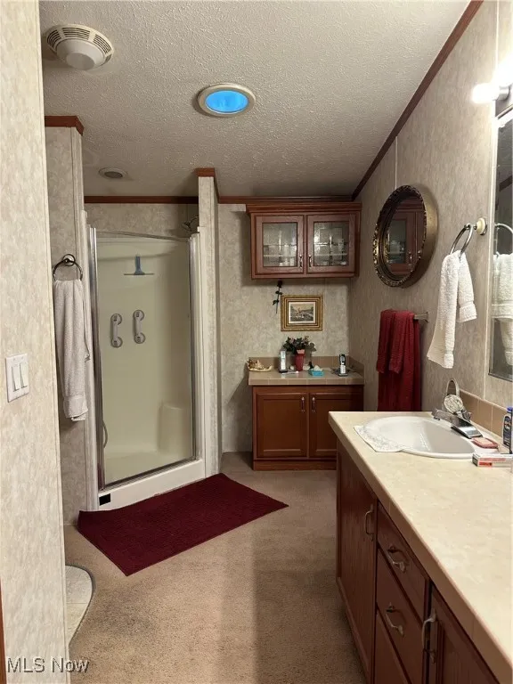Bathroom featuring ornamental molding, a textured ceiling, a shower stall, and vanity