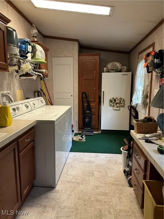 Laundry room with washing machine and clothes dryer, cabinet space, crown molding, and light carpet